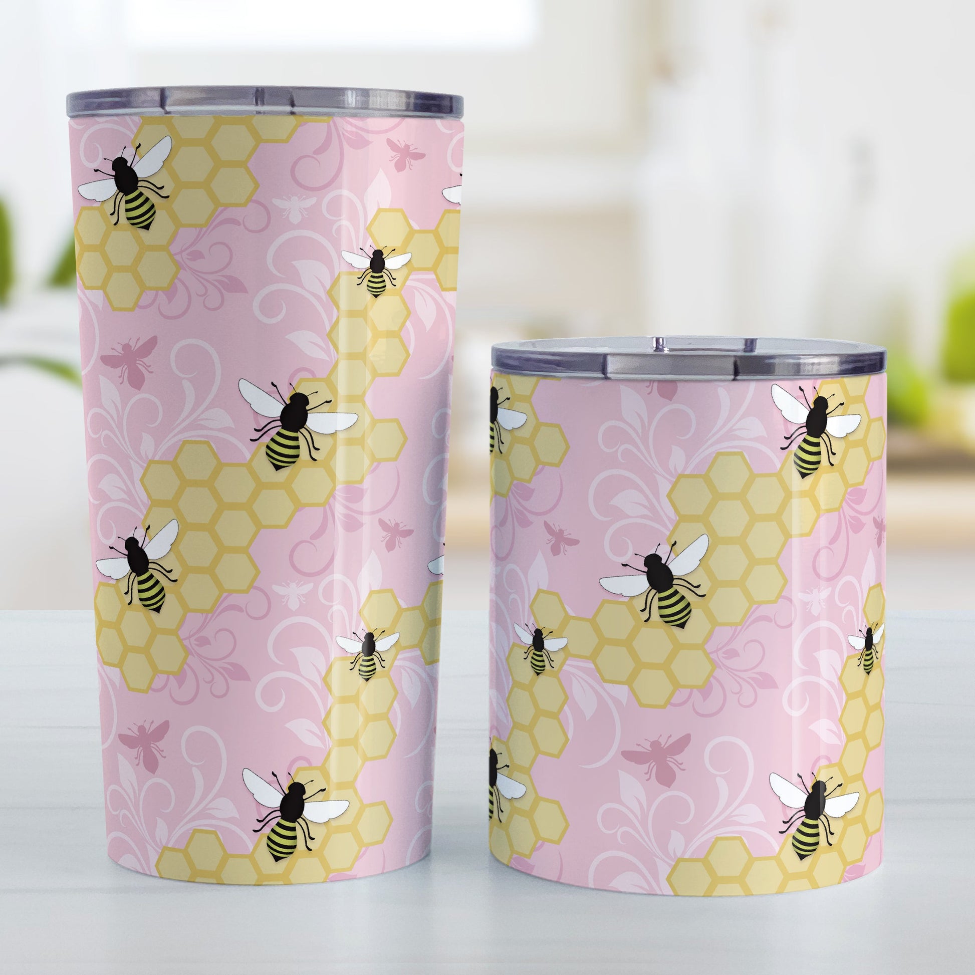 Pink Honeycomb Bee Tumbler Cup (20oz and 10oz, stainless steel insulated) at Amy's Coffee Mugs. Tumbler cups designed with a pattern of black and yellow bees on honeycomb lines over a pink flourish background that wraps around the cups. Photo shows both sized cups next to each other.