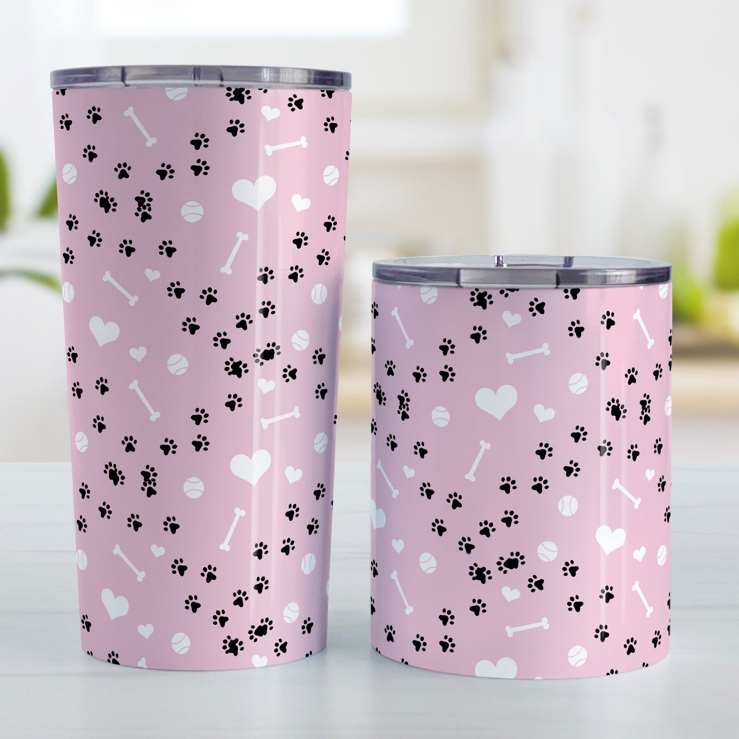 Puppy Run Pink Dog Tumbler Cup (20oz or 10oz) at Amy's Coffee Mugs. Stainless steel insulated tumbler cups designed with a pattern of chaotic tracks of puppy paw prints running around the cups with white dog bones, playing balls, and hearts over a light pink background that wraps around the cups. These cups are perfect for people who love puppy dogs, cute paw print designs, and the color pink. Photo shows both sized cups next to each other.