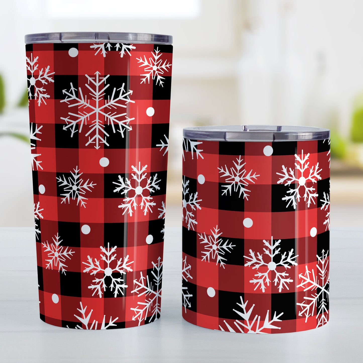 Red and Black Buffalo Plaid Snowflake Tumbler Cups (20oz and 10oz) at Amy's Coffee Mugs. Stainless steel insulated tumbler cups designed with a pattern of white snowflakes over a red and black buffalo plaid pattern that wraps around the cups. Photo shows both sized cups next to each other.