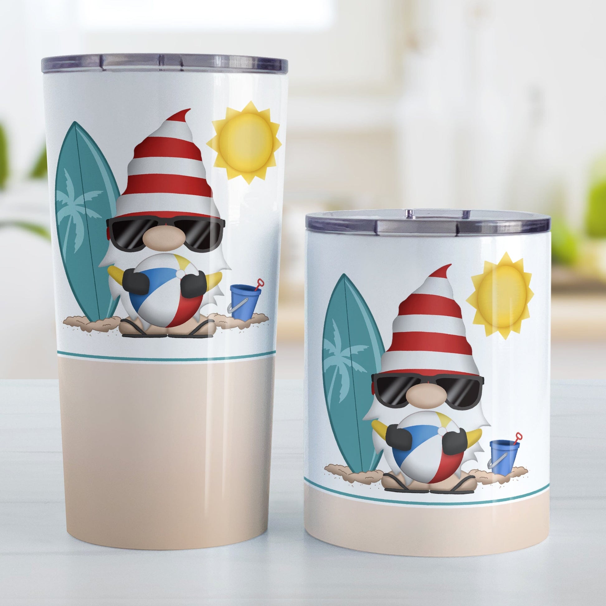 Summer Beach Gnome Tumbler Cups (20oz or 10oz) at Amy's Coffee Mugs. Stainless steel tumbler cups designed with an adorable gnome in sunglasses, holding a beach ball, with a surfboard and bucket in the sand on either side of him, and a bright yellow sun in the sky. Below the gnome is a sandy beige background color along the bottom of the cups. Photo shows both sized cups on a table next to each other.