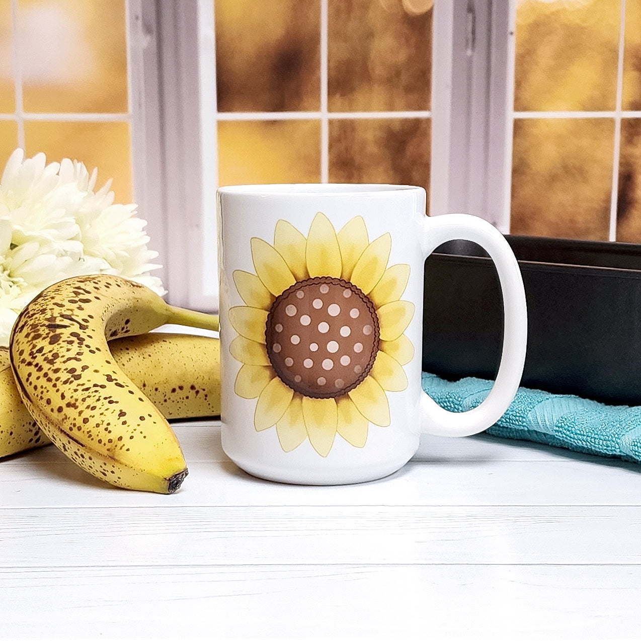 Cute 15oz sunflower mug on a table with bananas and a bread pan in front a fall window scene.