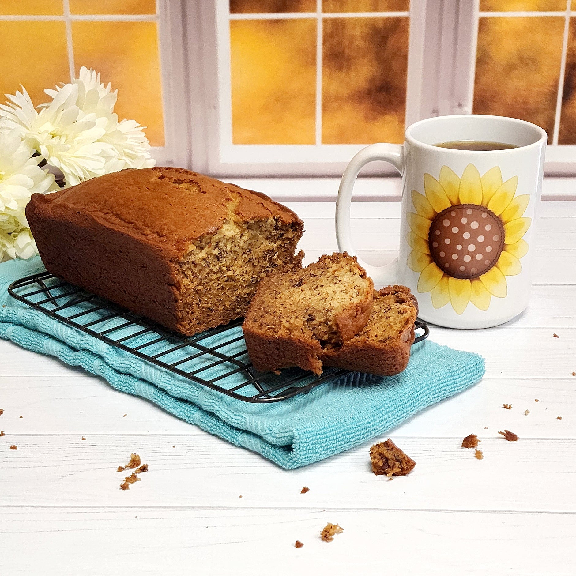 Cute 15oz sunflower mug on a table next to a banana bread loaf  in front a fall window scene.