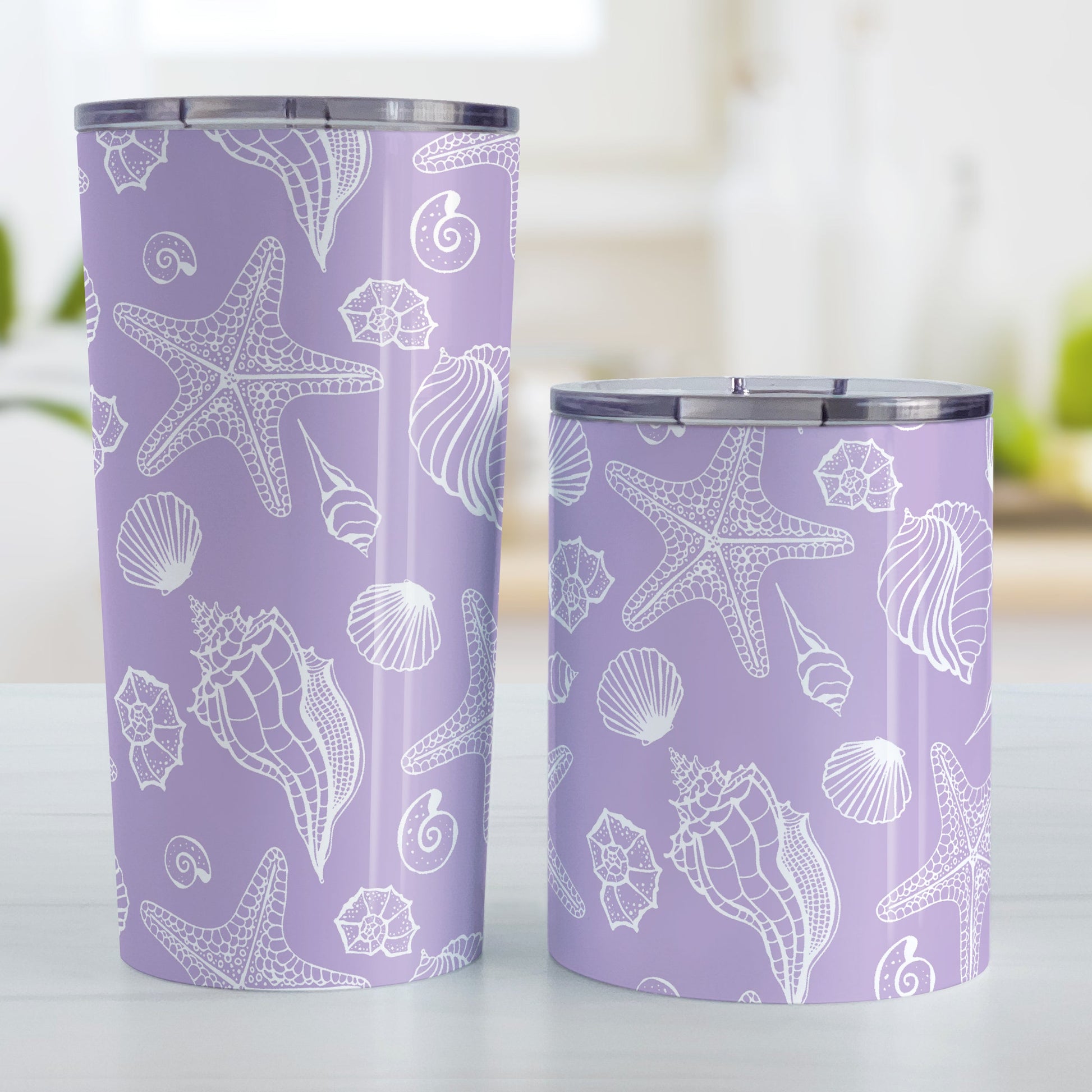 White Seashell Pattern Purple Beach Tumbler Cup (20oz and 10oz, stainless steel insulated) at Amy's Coffee Mugs. Tumbler cups designed with a white seashell line drawing pattern over a purple background that wraps around the cups. Photo shows both sized cups on a table next to each other. 