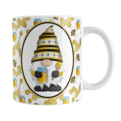 Yellow Gnome Honey Jar Bee Mug (11oz) at Amy's Coffee Mugs. A ceramic coffee mug designed with an adorable gnome wearing a yellow bee-themed hat and holding a honey jar and honey dipper in a white oval over a pattern background that wraps around the mug to the handle with bees, honey jars, honey dippers, and honeycomb.