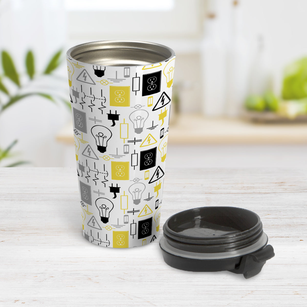 Yellow Gray Electrical Electrician Travel Mug (15oz) at Amy's Coffee Mugs. A stainless steel travel mug designed with an electrical pattern with light bulbs, wall sockets, plugs, fuses, and other electricity symbols in yellow, gray, and black colors. This travel mug is perfect for people who work a trade as an electrician or love working with electronics. Photo shows the cup open with the lid on the table beside it. 